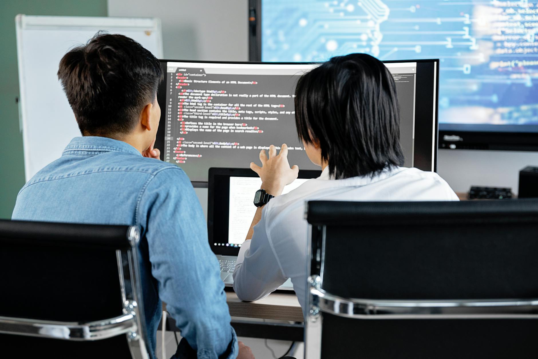 Dwóch programistów omawia kod na monitorze w biurowym open space