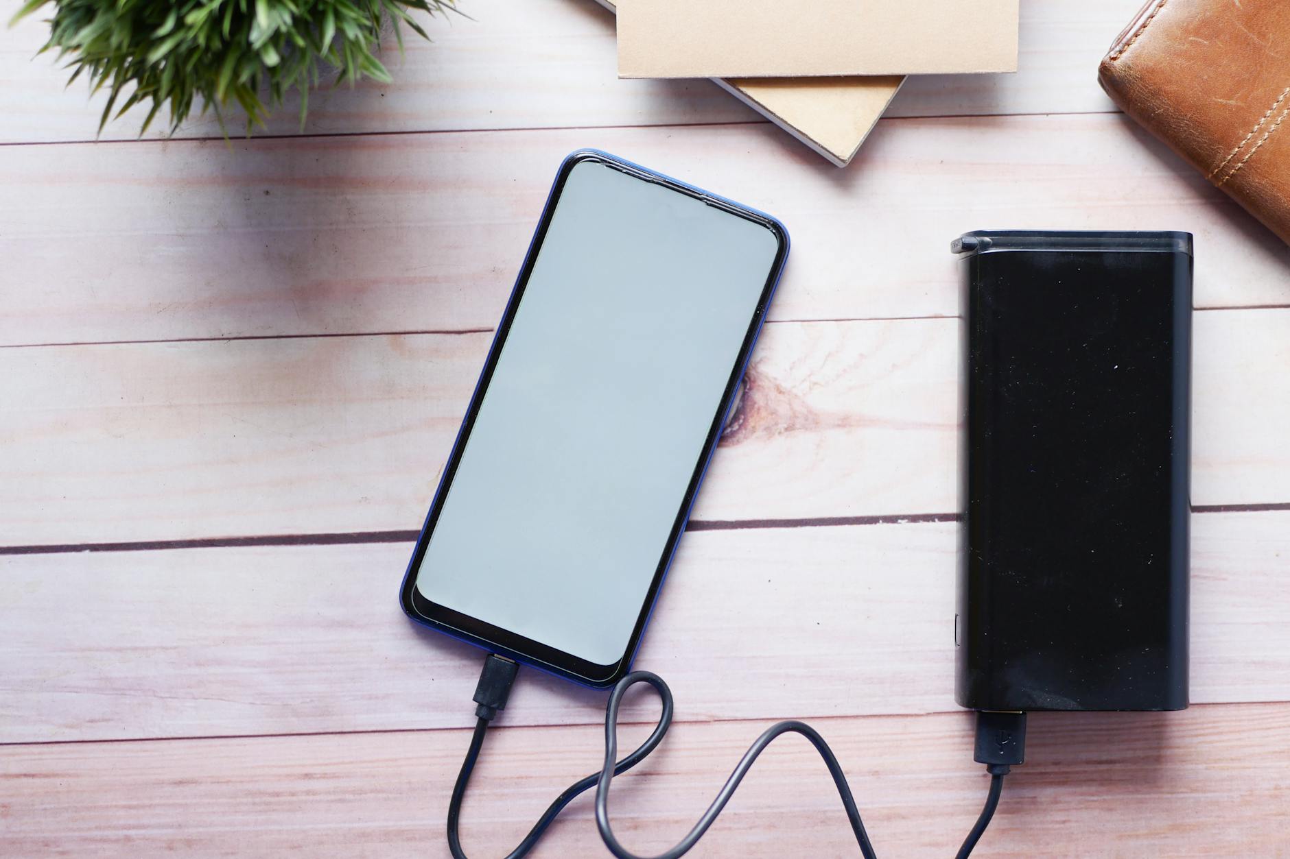 Smartfon ładowany z powerbanku na drewnianym biurku