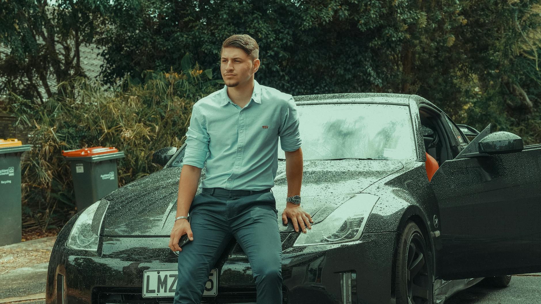 Młody mężczyzna w garniturze oparty o luksusowy sportowy samochód