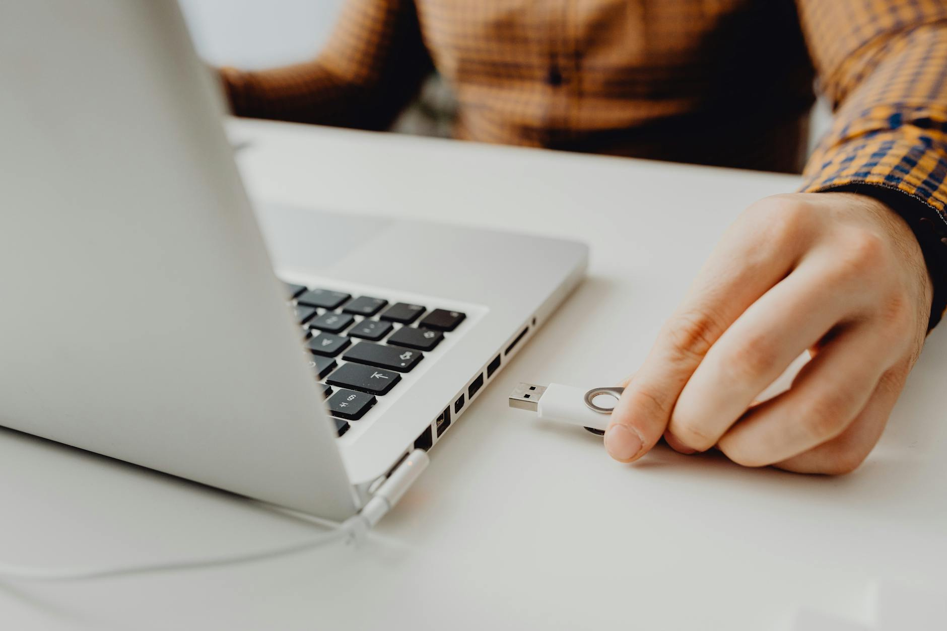Osoba podłączająca pendrive do laptopa podczas pracy z danymi