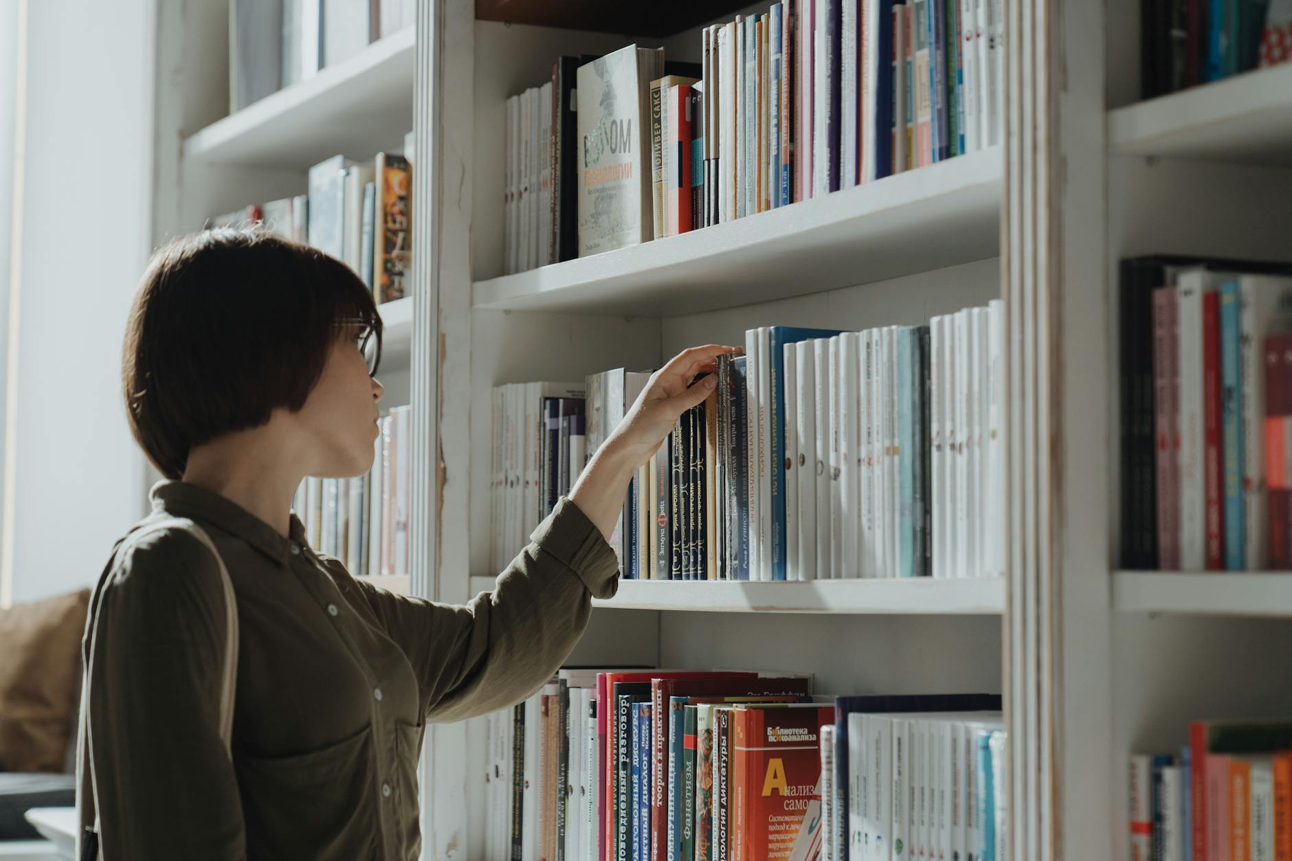 Kobieta przegląda książki na półce w nowoczesnej bibliotece