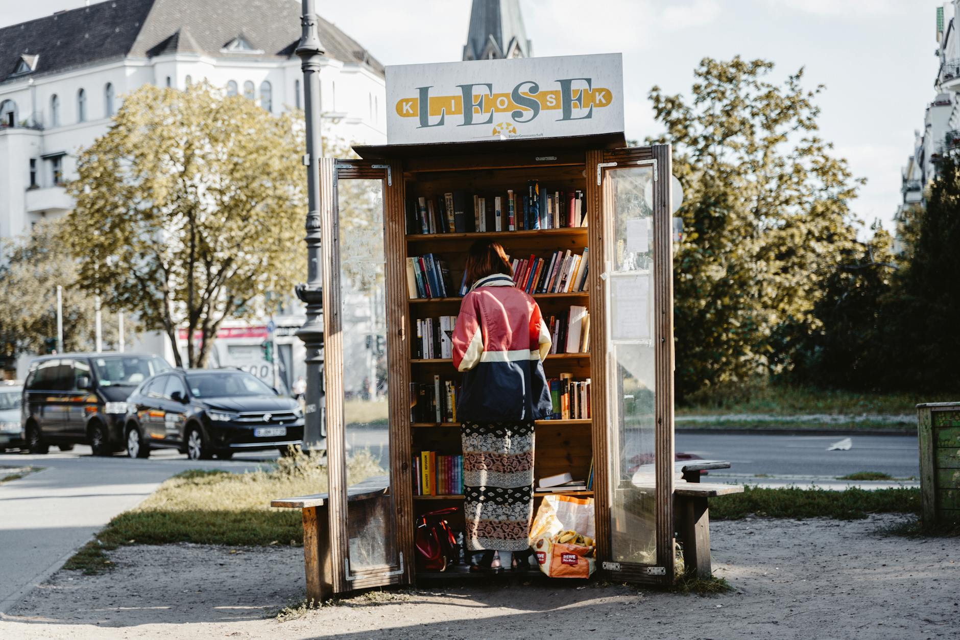 Osoba sięga po książkę z plenerowej biblioteczki przy ulicy
