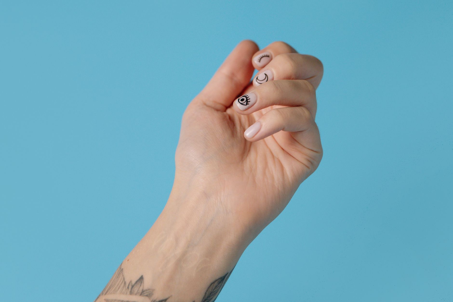 Zbliżenie wytatuowanej dłoni z pastelowym manicure na błękitnym tle