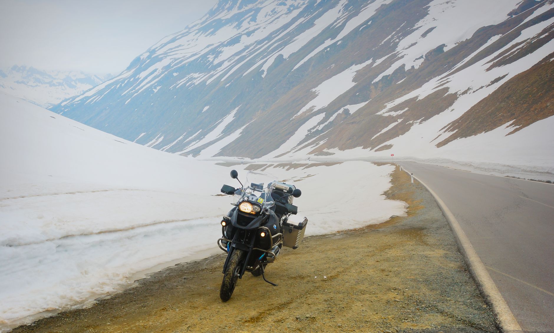 Motocykl przy ośnieżonej alpejskiej szosie na górskiej przełęczy Motocykl przy ośnieżonej alpejskiej szosie na górskiej przełęczy