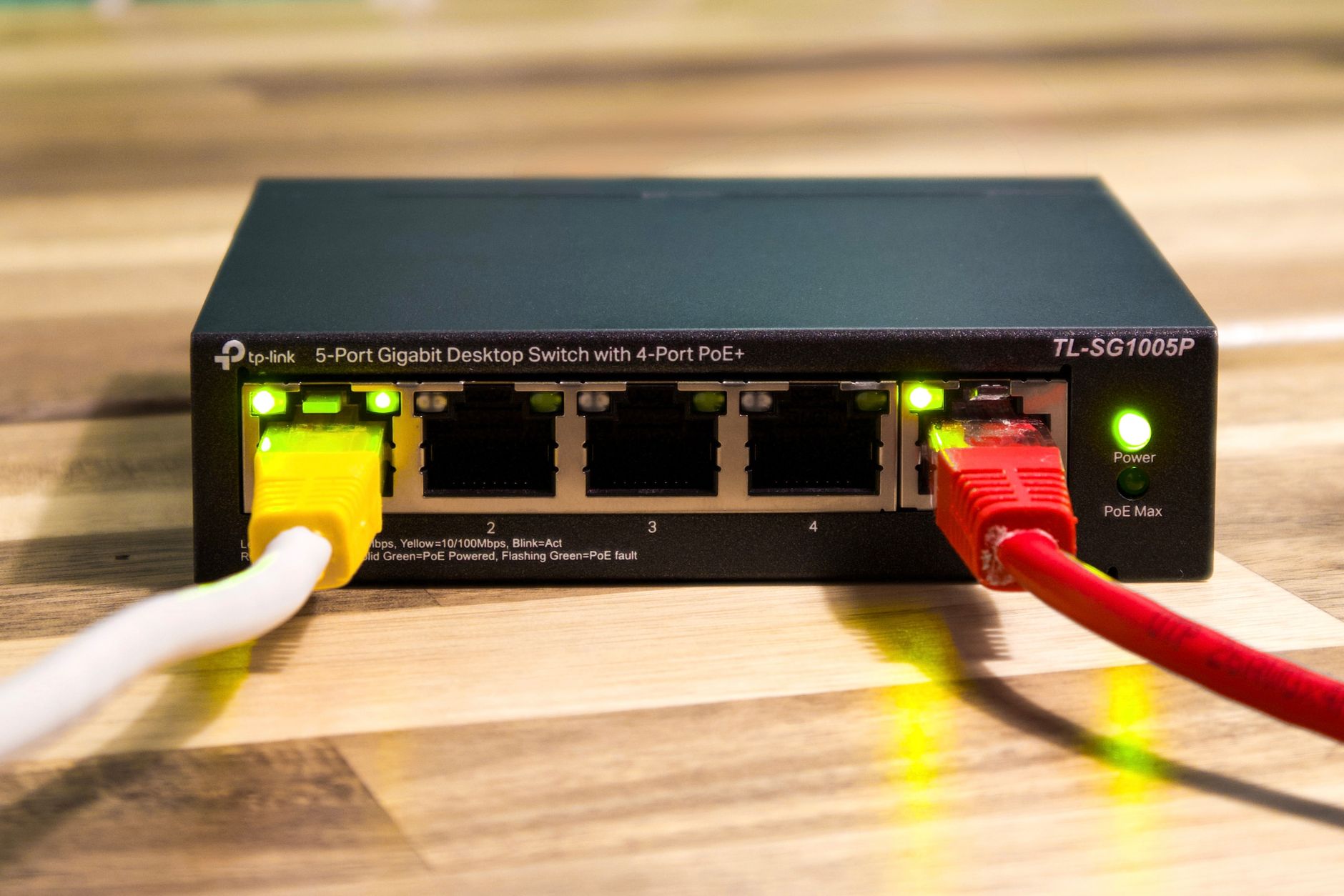 Switch sieciowy do domu i SOHO: 1G czy 2.5G, PoE czy bez? Switch TP-Link z podłączonymi żółtymi, czerwonymi i białymi kablami Ethernet